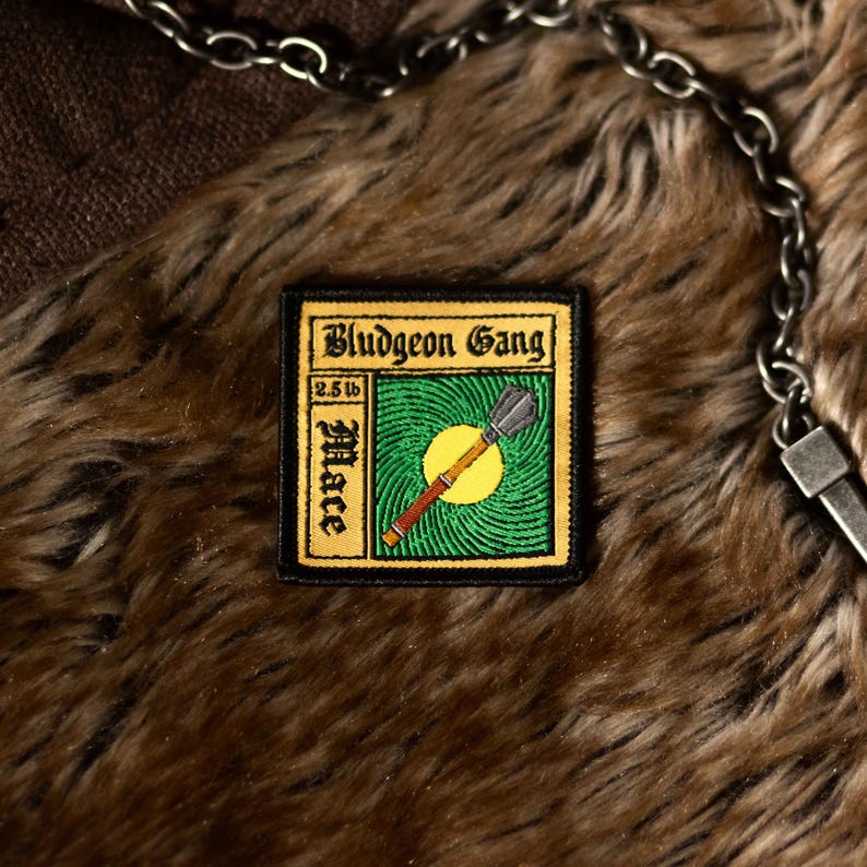 May include: A brown and black embroidered patch with the text "Bludgeon Gang" and "2.5 lb Mace" in a yellow box. The patch features a green background with a yellow sun and a brown and black mace.