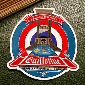 May include: A blue and red circular sticker with a graphic of a guillotine with a guitar in it. The text on the sticker reads "National Tour 1792" and "Guillotine Heads Will Roll".