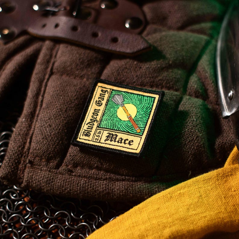 May include: A yellow and green embroidered patch with the text "Bludgeon Gang 2.5lb Mace" and a graphic of a mace.