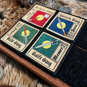 May include: Four embroidered patches with different weapon designs and names. The patches are beige with black text and are arranged in a square shape. The patches are: Bludgeon Gang, Bolearm Gang, Blade Gang, and Knife Gang.