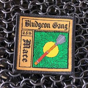 May include: A black and tan embroidered patch with the text "Bludgeon Gang" and "2.5 lb Mace" in a stylized font. The patch features a green and yellow background with a cartoon illustration of a mace.