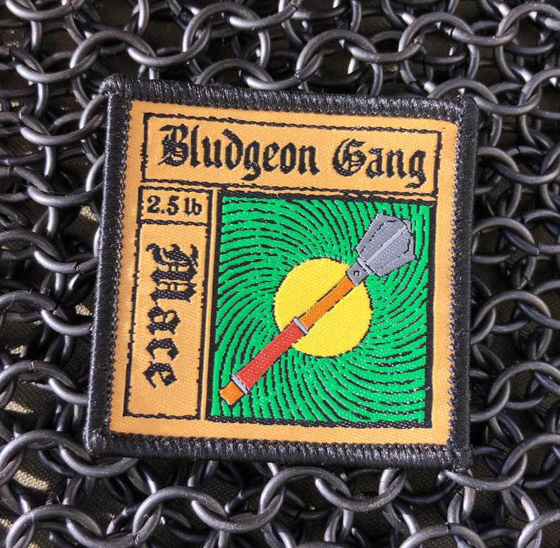 May include: A black and tan embroidered patch with the text "Bludgeon Gang" and "2.5 lb Mace" in a stylized font. The patch features a green and yellow background with a cartoon illustration of a mace.