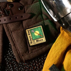 May include: A brown fabric patch with a green and yellow design. The patch features a mace weapon and the text "Bludgeon Gang 2.5.10 Mace".