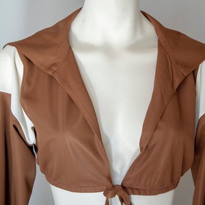 May include: A brown and white cropped jacket with a long sleeve and a tie at the waist.