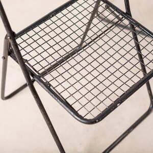 May include: Black metal folding chair with a wire mesh seat. The chair is made of sturdy metal and has a simple, modern design.