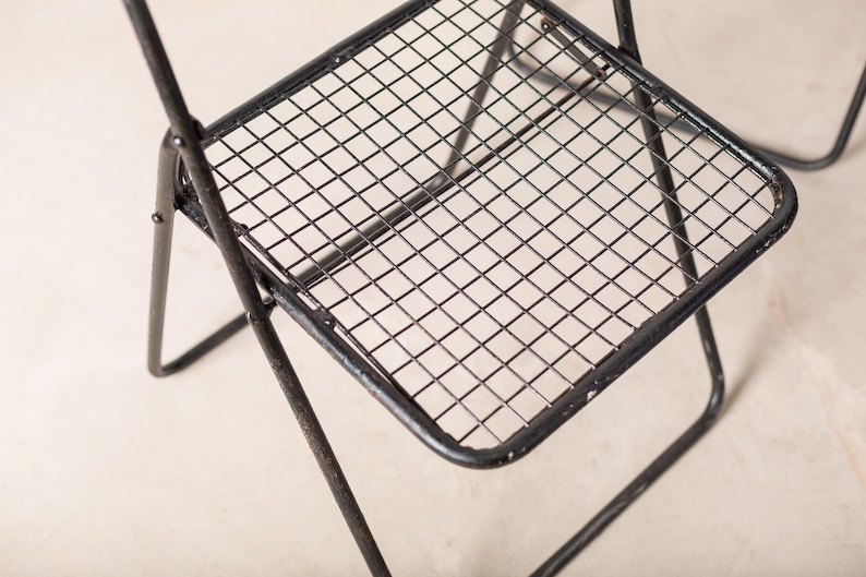 May include: Black metal folding chair with a wire mesh seat. The chair is made of sturdy metal and has a simple, modern design.