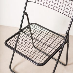 May include: Black metal folding chair with a wire mesh seat and back. The chair is in a folded position.