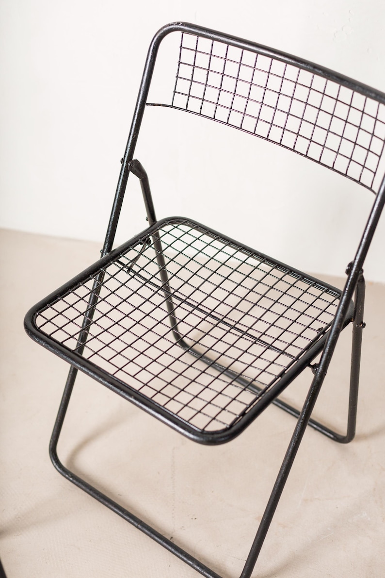 May include: Black metal folding chair with a wire mesh seat and back. The chair is in a folded position.