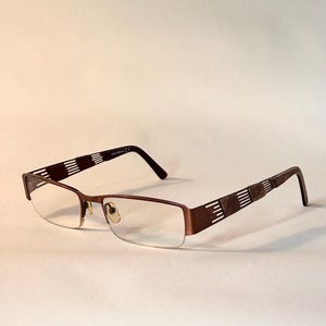 May include: Brown semi-rimless spectacles featuring rectangular lenses and metal frames. The temples display a decorative pattern of alternating solid brown segments and vertical cut-out lines, with clear nose pads and curved temple tips.