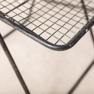 May include: Close-up of a black metal chair with a wire mesh seat. The chair is made of sturdy metal and has a simple, industrial design.