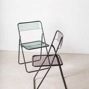 May include: Two black metal folding chairs with a wire mesh seat and back. The chairs are in a white room.