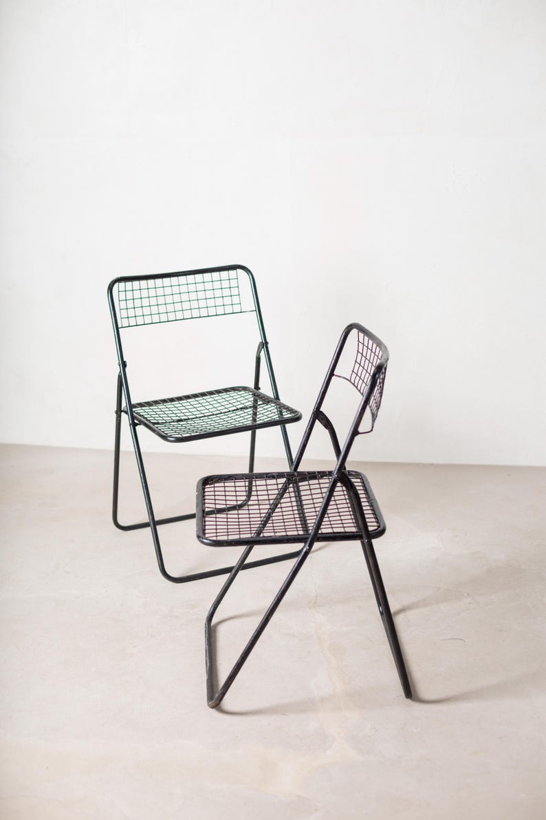 May include: Two black metal folding chairs with a wire mesh seat and back. The chairs are in a white room.