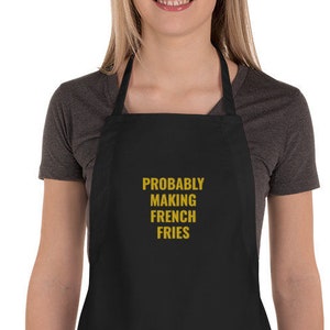 May include: Black apron with a large pocket and adjustable straps. The apron has the text "PROBABLY MAKING FRENCH FRIES" in gold lettering.