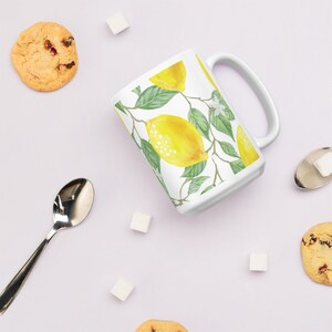 May include: White ceramic mug with a lemon and leaf design. The mug has a handle and is filled with a white liquid.