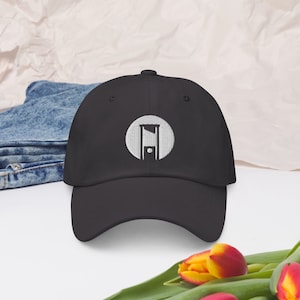 May include: A black baseball cap with a white embroidered circle containing a guillotine silhouette.