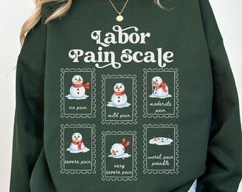 May include: A dark green sweatshirt with the text "Labor Pain Scale" and illustrations of snowmen depicting different levels of pain. The sweatshirt is a Forrest Green color.