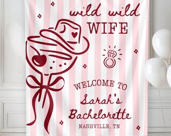 May include: A rectangular fabric banner with vertical light pink and white stripes. The design features dark red text reading wild wild WIFE, WELCOME TO Sarah's Bachelorette, and NASHVILLE, TN, alongside a martini glass with a cowboy hat and a ring.
