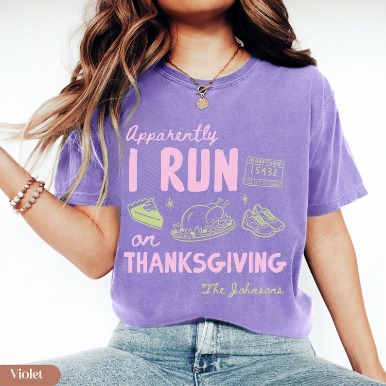 K&ouml;nnte beinhalten: Ein violettes Kurzarm-T-Shirt mit dem Text "Apparently I RUN on THANKSGIVING" in Pink und Wei&szlig;. Die Grafik zeigt ein St&uuml;ck Kuchen, einen gebratenen Truthahn, ein Paar Laufschuhe und eine Marathon-Startnummer 15432 in hellem Gr&uuml;n.