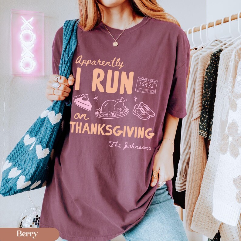 K&ouml;nnte beinhalten: Ein beerenfarbenes T-Shirt mit dem Text "Apparently I RUN on THANKSGIVING" in hellem Orange sowie grafischen Illustrationen eines St&uuml;cks Kuchen, eines gebratenen Truthahns, eines Laufschuhpaars und einer Marathon-Startnummer "15432".