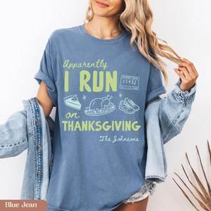 K&ouml;nnte beinhalten: Ein blaues T-Shirt mit dem Text "Apparently I RUN on THANKSGIVING" in Hellgr&uuml;n. Die Grafik zeigt ein St&uuml;ck Kuchen, einen gebratenen Truthahn, ein Paar Laufschuhe und eine Marathon-Startnummer mit der Aufschrift "15432". Darunter steht "The Johnsons".