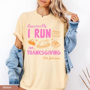 K&ouml;nnte beinhalten: Ein butterfarbenes T-Shirt mit dem rosa Text Apparently I RUN ON THANKSGIVING, einer Marathon-Startnummer 15432, einem St&uuml;ck Kuchen, einem gebratenen Truthahn, Laufschuhen und dem kursiven Text The Johnsons in Orange.