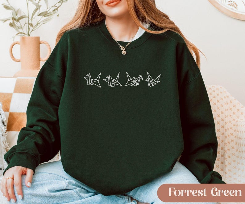 May include: A dark green sweatshirt with a white origami crane design. The sweatshirt is a solid color with a crew neck and long sleeves. The text "Forrest Green" is at the bottom of the image.