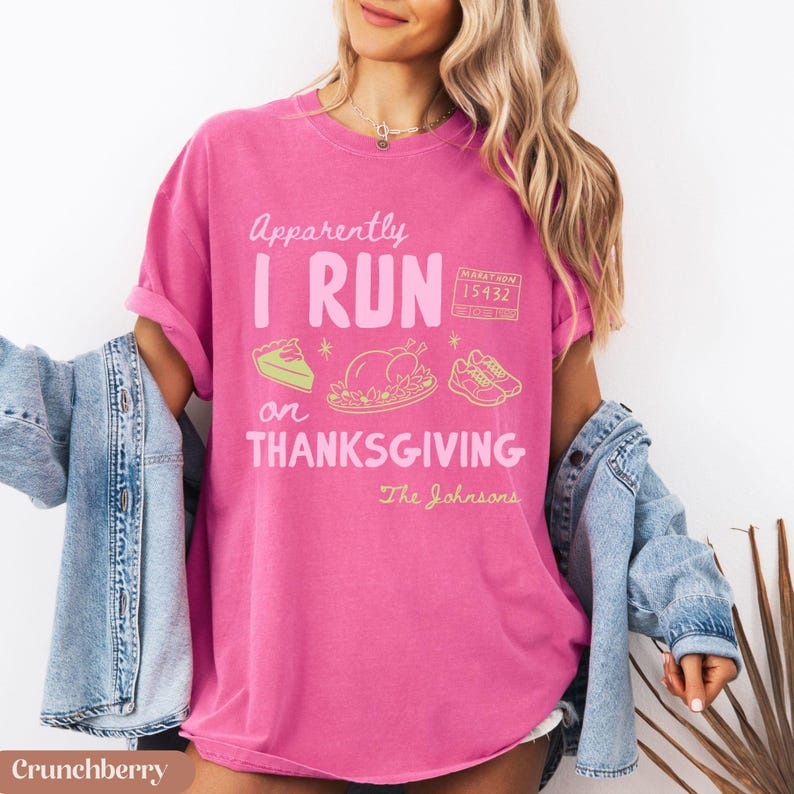 K&ouml;nnte beinhalten: Ein leuchtend pinkfarbenes Kurzarm-T-Shirt mit dem Text "Apparently I RUN on THANKSGIVING" in Wei&szlig; und Hellrosa. Die Grafik zeigt ein St&uuml;ck Kuchen, einen gebratenen Truthahn, eine Marathon-Startnummer 15432 und Laufschuhe in Gelb.