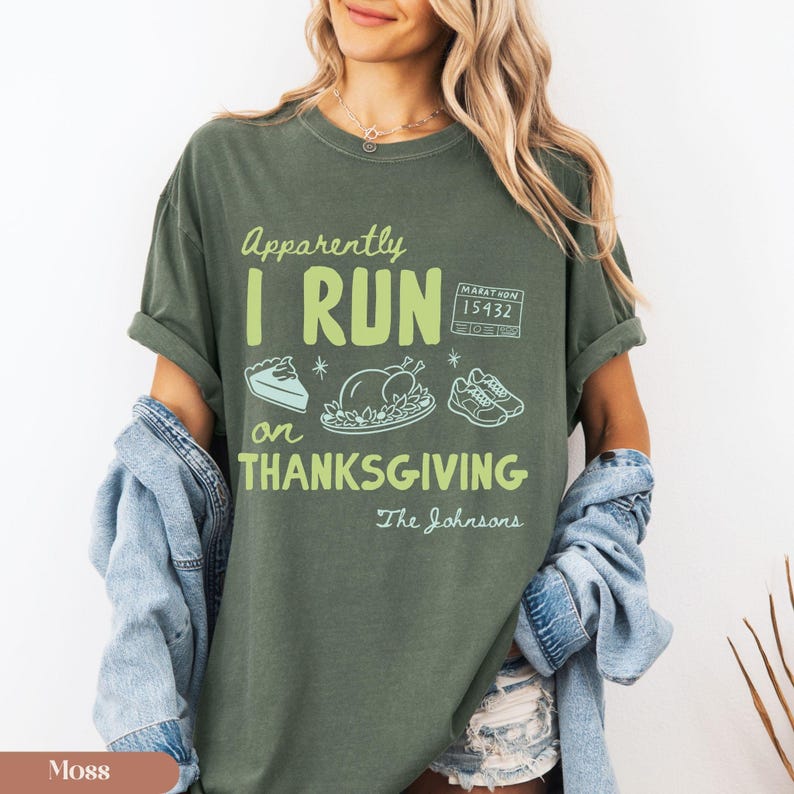 K&ouml;nnte beinhalten: Ein olivgr&uuml;nes Kurzarm-T-Shirt mit hellgr&uuml;nem Text, der Apparently I RUN on THANKSGIVING lautet. Das Design enth&auml;lt Strichzeichnungen eines St&uuml;cks Kuchen, eines gebratenen Truthahns, Laufschuhen, einer Startnummer und dem Text The Johnsons.