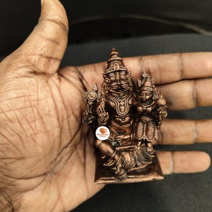 Puede incluir: Una estatua de color bronce de una deidad con un tocado detallado y múltiples brazos. La estatua se sostiene en una mano, mostrando su intrincado diseño y estilo tradicional. La estatua mide aproximadamente 7,6 cm de altura.