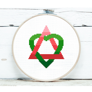 May include: A cross-stitch embroidery hoop with a green and red heart design. The heart is made up of two overlapping triangles, one red and one green.