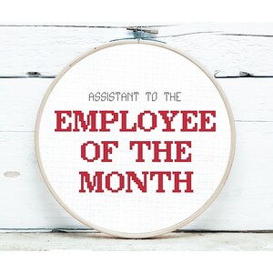 以下が含まれることがあります： 赤いピクセル文字で「Assistant to the Employee of the Month」と書かれた白い刺繍枠です。