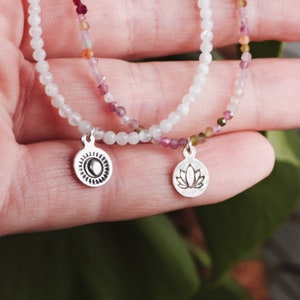 Peut inclure: Deux bracelets délicats en perles avec des breloques. Un bracelet est blanc avec un charme soleil, l'autre est multicolore avec un charme fleur de lotus.