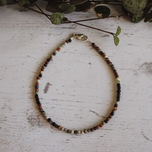 May include: A beaded bracelet with a silver clasp. The beads are a mix of brown, black, gray, and white.