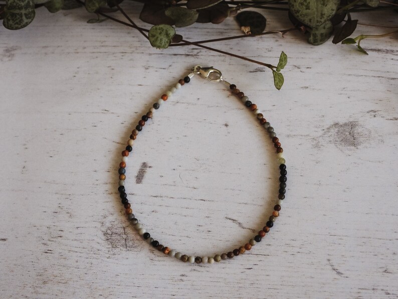 May include: A beaded bracelet with a silver clasp. The beads are a mix of brown, black, gray, and white.