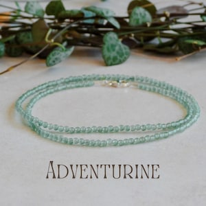 May include: A delicate green aventurine gemstone necklace with a silver clasp. The necklace is made of small, round beads and is layered for a subtle, elegant look.