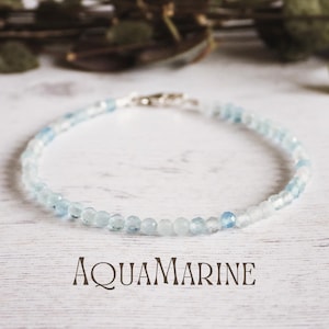 Puede incluir: Un delicado brazalete de piedras preciosas de aguamarina con un cierre de plata. El brazalete está hecho de pequeñas cuentas redondas que están graduadas en tamaño, con las cuentas más grandes en el centro del brazalete. Las cuentas son de color azul claro, con un ligero brillo.