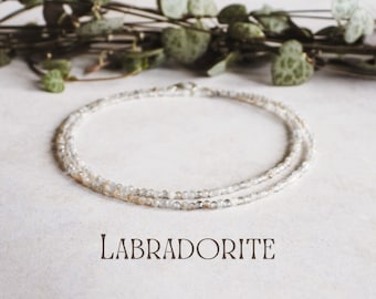 Puede incluir: Un delicado collar de capas hecho con pequeñas cuentas de labradorita iridiscente. El collar es blanco con un brillo sutil.