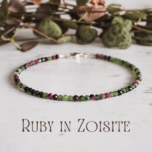 May include: A delicate bracelet made with green, black, and pink gemstone beads. The bracelet is made with small, round beads and has a silver clasp. The text "RUBY IN ZOISITE" is printed below the bracelet.