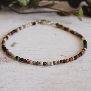 May include: A multi-colored beaded necklace with brown, black, white, and grey beads.