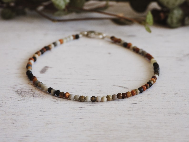 May include: A multi-colored beaded necklace with brown, black, white, and grey beads.