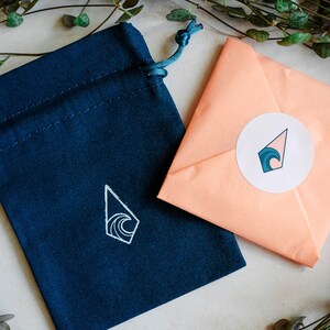 May include: A blue fabric pouch with a white wave design and a peach-colored envelope with a white circle sticker featuring a blue wave design.