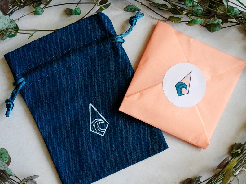 May include: A blue fabric pouch with a white wave design and a peach-colored envelope with a white circle sticker featuring a blue wave design.