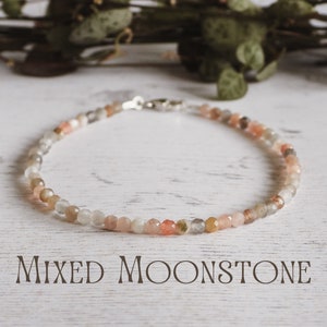 May include: A delicate necklace made with mixed moonstone beads in shades of white, grey, and pink. The necklace is strung on a silver chain and has a simple clasp.