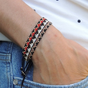 May include: Two beaded bracelets on a person's wrist. The bracelets are made with black, white, red, and brown beads. The bracelets are tied with black string.