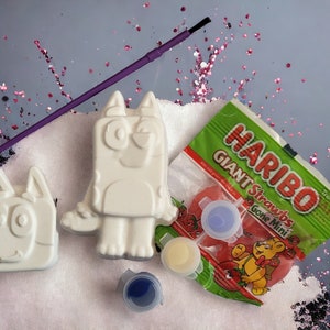 May include: A children's craft set with two unpainted dog figurines, paint pots, a paintbrush, and a bag of Haribo Giant Straws. The kit includes red, yellow, and blue paint. The Haribo bag is green with red sweets.