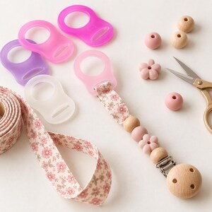 Peut inclure: Une attache-sucette avec une sangle en tissu floral, des perles en bois et en silicone, et une pince en bois. L'ensemble comprend quatre anneaux de sucette en silicone translucide violet, rose et transparent, ainsi que des perles et des ciseaux.