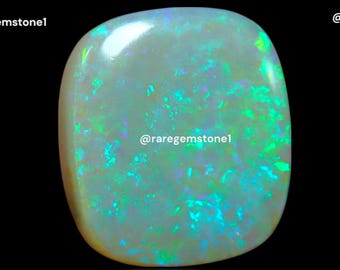 May include: A polished, oval-shaped opal gemstone with a creamy white base and vibrant flashes of green and blue. The gemstone is set against a black background, highlighting its iridescent play-of-color. The text "@raregemstone1" is visible.
