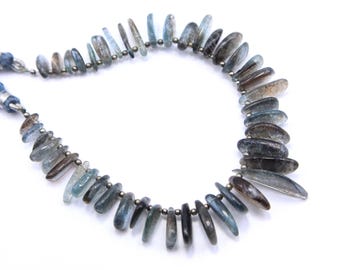 May include: A strand of blue aquamarine gemstone beads, each bead is a long, thin, teardrop shape. The beads are strung on a silver wire.
