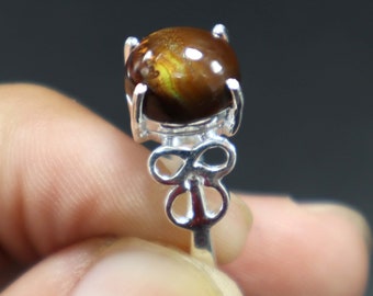 May include: A silver ring with a brown and yellow agate gemstone set in a prong setting. The ring band features a delicate, openwork design.
