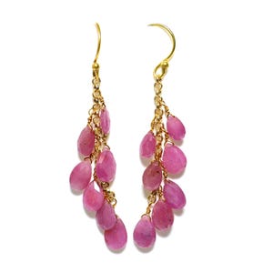 May include: A pair of gold earrings with pink gemstone drops. The earrings are made with multiple strands of gold chain and feature a cascading design of pink gemstones.